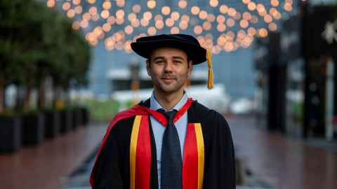 Moritz in PhD regalia in front of fountain and lights in downtown Auckland