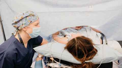 Esther in midwife scrubs at the bedside of a woman giving birth (her niece)