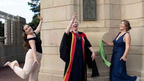 Esther throws her PhD hat in the air and her daughters celebrate in The Domain, Auckland