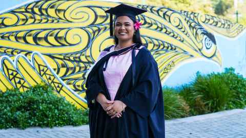 Head and shoulders of graduate Mary Lale in graduation regalia against a colourful mural outside Spark Arena.