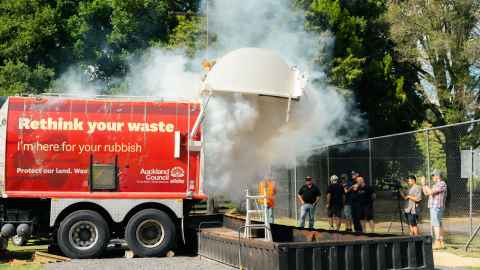A rubbish truck emits a large plume of smoke from its rear door.