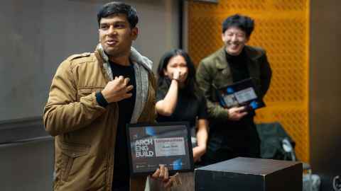 A student holds up a certificate at a podium, with two fellow team members cheering him on behind him.