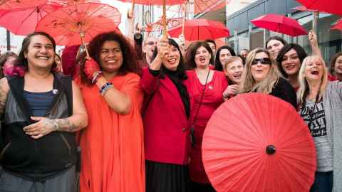 Lots of women with red umbrellas looking happy and festive.