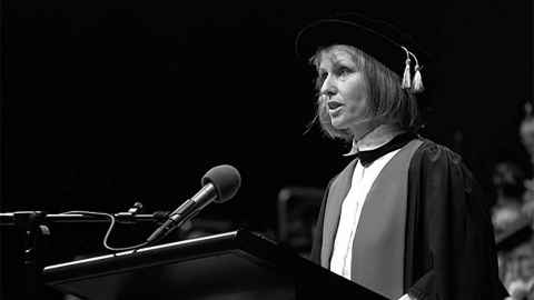 Vivienne Gray wearing academic regalia at the podium during a graduation ceremony.