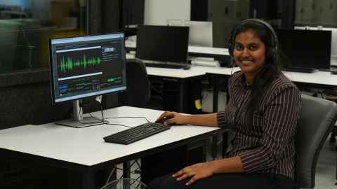 Himashi Rathnayake sits at a computer desk with waveforms
