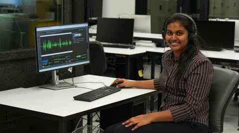 Himashi Rathnayake sits at a computer desk with waveforms