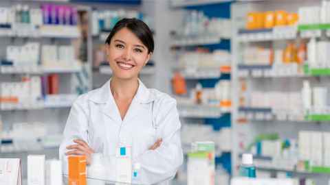 Female pharmacist behind counter, smiling at camera
