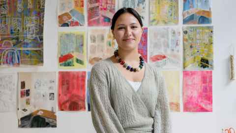 Assistant curator Audrey Goggin wearing a fawn jersey and a bead necklace against a colourful backdrop of images.