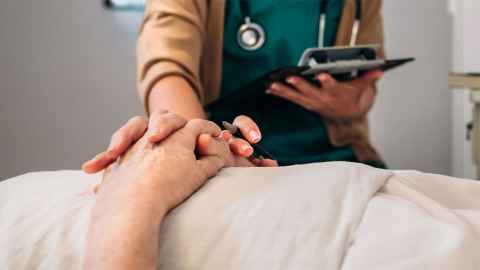 Image of hand of healthcare worker, holding hand of person in hospital bed