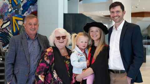 Alex and her family, father, mother, partner and young daughter, standing inside the Aotea Centre on graduation day.