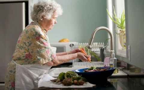 Older woman in apron washing carrots at a sink