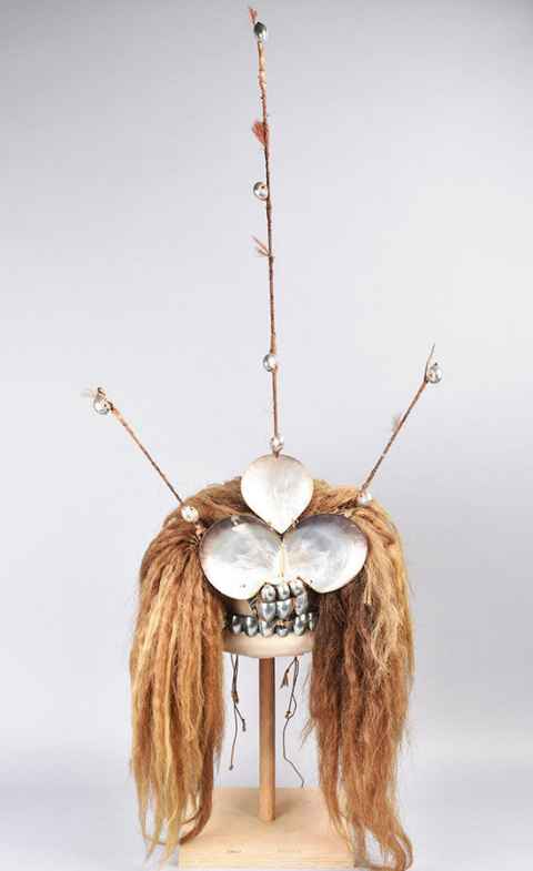 Tuiga headdress. made of bunches of yellow (dyed) human hair. The middle section consists of three pearl shells strung together with vegetable fibre cord, below this are three rows of nautilus shells. The top part of the headdress is made of three projecting spikes covered with fibre or possibly barkcloth, two nautilus shells are attached to the outer spikes, and four nautilus shells (fuiono) are attached to the central spike. Red feathers decorate all three spikes. © The Trustees of the British Museum. Shared under a Creative Commons Attribution-NonCommercial-ShareAlike 4.0 International (CC BY-NC-SA 4.0) licence.