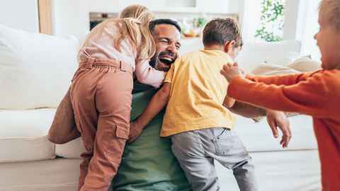 Father playing on couch with three kids, laughing