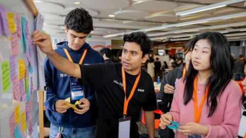 Three students adding post-it notes to a white board