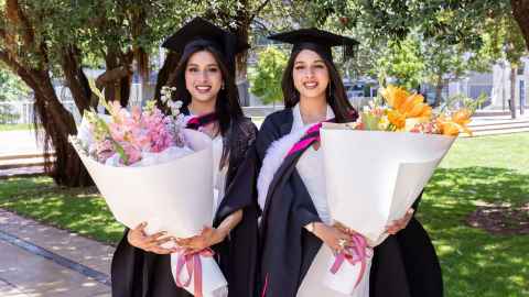 Sanumi and Sanuthi Ranasinghe in their graduation garb holding large bunches of flowers.
