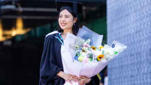 Grace Su in graduation garb and carrying a bunch of flowers.