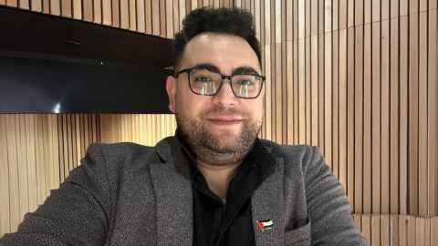 PhD candidate Saleh Albalawi wearing a black shirt and grey blazer against a wooden panelled wall.