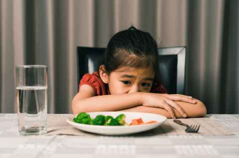 A child looking despairingly at a  plate of brocolli and carrots. 