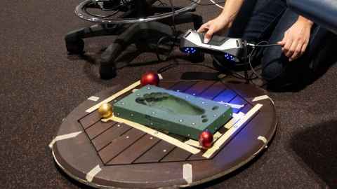 Scanner has a wooden base and a raised green footprint part where the child's foot goes. Sara holds the portable scanner