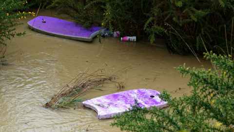 Two purple body boards have come to rest in muddy floodwater. Two plastic drink bottles can also be seen alongside.