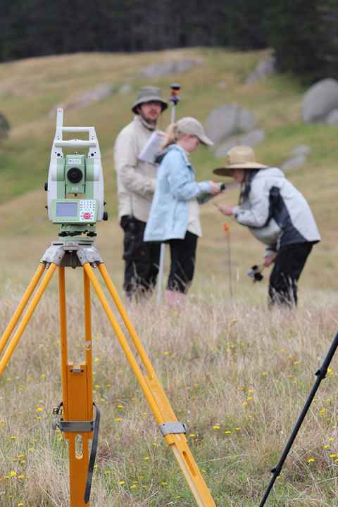Three students standing in a group with survey equipment in the foreground. Photo: Tim Mackrell