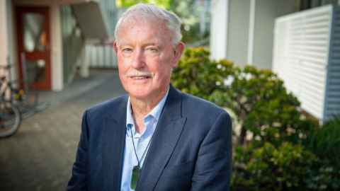 A head shot of Emeritus Professor Ralph Cooney. He is pictured outside and wears a navy blue jacket over a pale blue shirt.