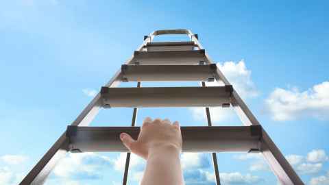 Lower perspective of hand holding rung of middle ladder, with sky in background. 