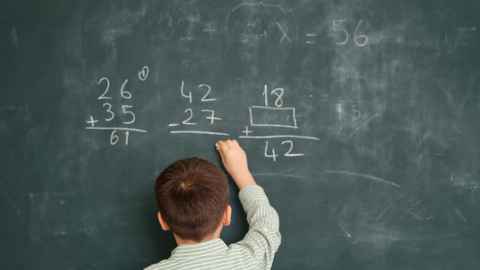 View of back of young boy solving maths problems on a blackboard 