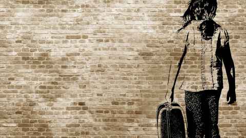 Stencil painting on brick wall of girl carrying suitcase. 