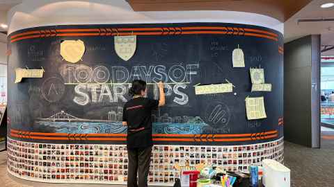 Rosanna in front of large blackboard chalking "100 Days of Start-ups"