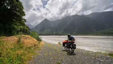 A single cyclist, pausing alongside a laden touring bike, on the banks of the Haast river valley.