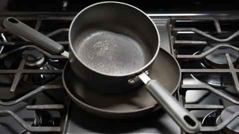 A non-stick frying pan, with a saucepan on top of it. Both are in the centre of a gas stove.