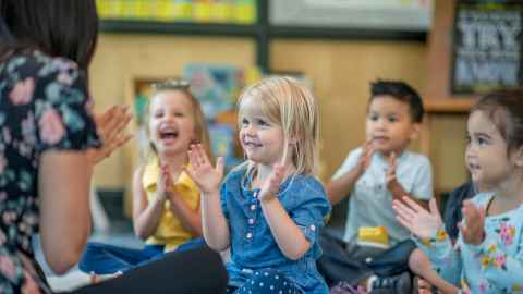 Image of young children laughing and clapping, with teacher. 