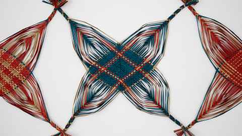 Woven geometric artwork in red, blue, and natural fibres, featuring a central star-shaped pattern against a white background.