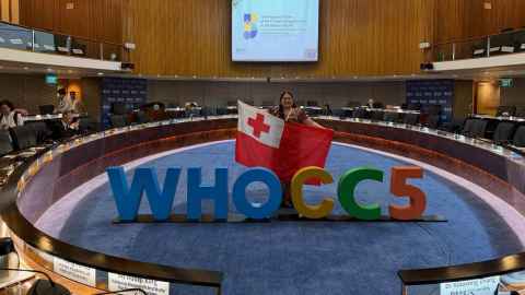 Nalei Taufa in the centre of the circular WHOCC5 meeting room, holding the flag of Tonga