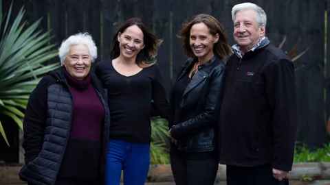 Kelly Klink with her parents and twin sister against a green backdrop.