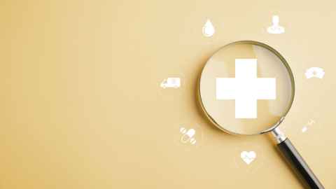 Concept image of magnifying glass over a hospital cross, sounded by images of heart, ambulance etc. 