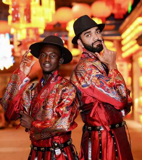 Nimish Milan Singh and friend in traditional Chinese clothing, rich, red patterned kimonos and black brimmed hats.