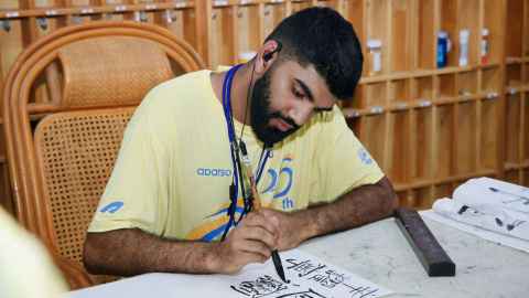 Nimish Milan Sing practising Chinese calligraphy with an ink pen wearing a yellow t-shirt.