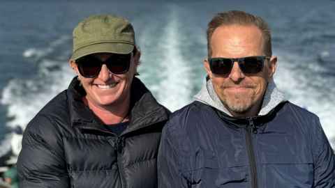 Luke and Suzanne on a boat wearing sunglasses with warm jackets and the sea in the background.