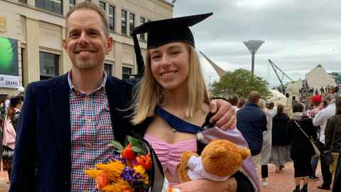 Luke Goode and daughter Aggie who is graduating in Wellington, wearing a pink dress, academic regalia and holding bouquet of flowers and a teddy.