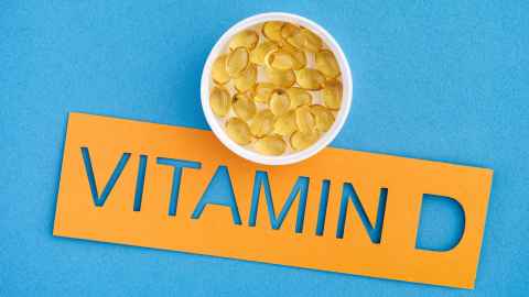 Word Vitamin D cut out of orange paper, with small bowel of supplements