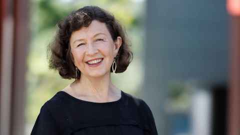 Associate Professor Kathy Smits wearing a black top against a blurred window background with greenery behind.