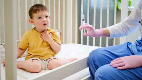 Worried looking boy with doctor holding injection in front of him 