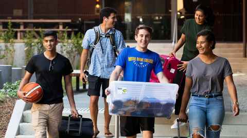 Young people walking down stairs, carrying sports equipment and luggage.