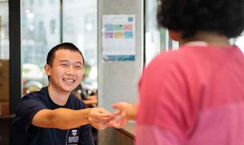 Resident is sitting a table looking up at an Accommodation staff member and speaking