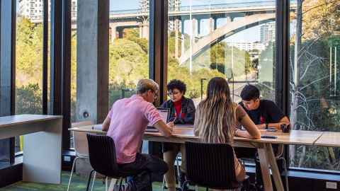 Group of four people sitting at a table studying. They are next to wall to wall windows overlooking Grafton Bridge and the motorway. 