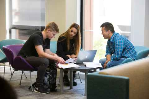 Three students huddled around a laptop and sitting 