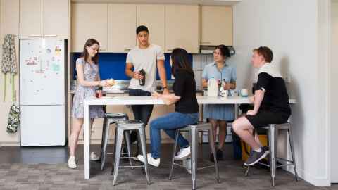 Group of five people around a high kitchen table chatting