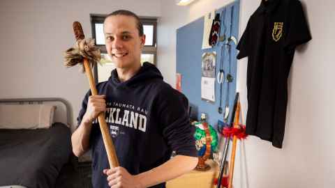 Nīkau holds his taiaha proudly with both hands.